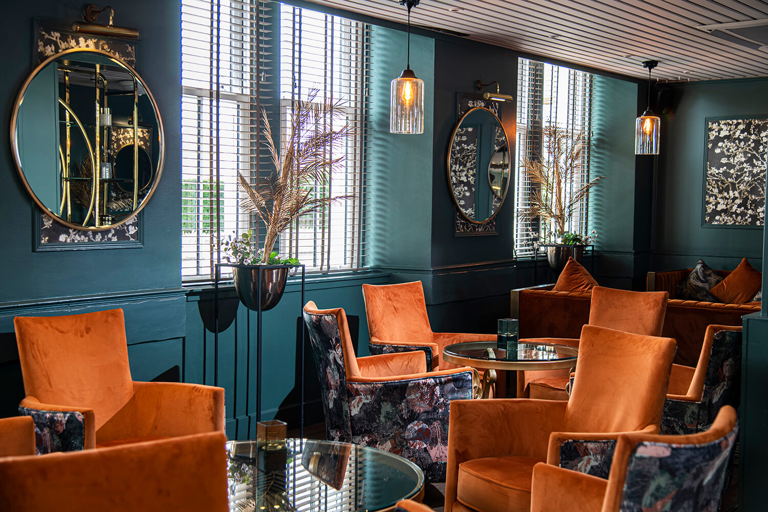 Interior of hotel lounge. There are orange chairs and the walls are turquoise. There are warm lights on the walls and artificial gold ferns. By Glasgow hospitality and leisure photographers Blink Imaging