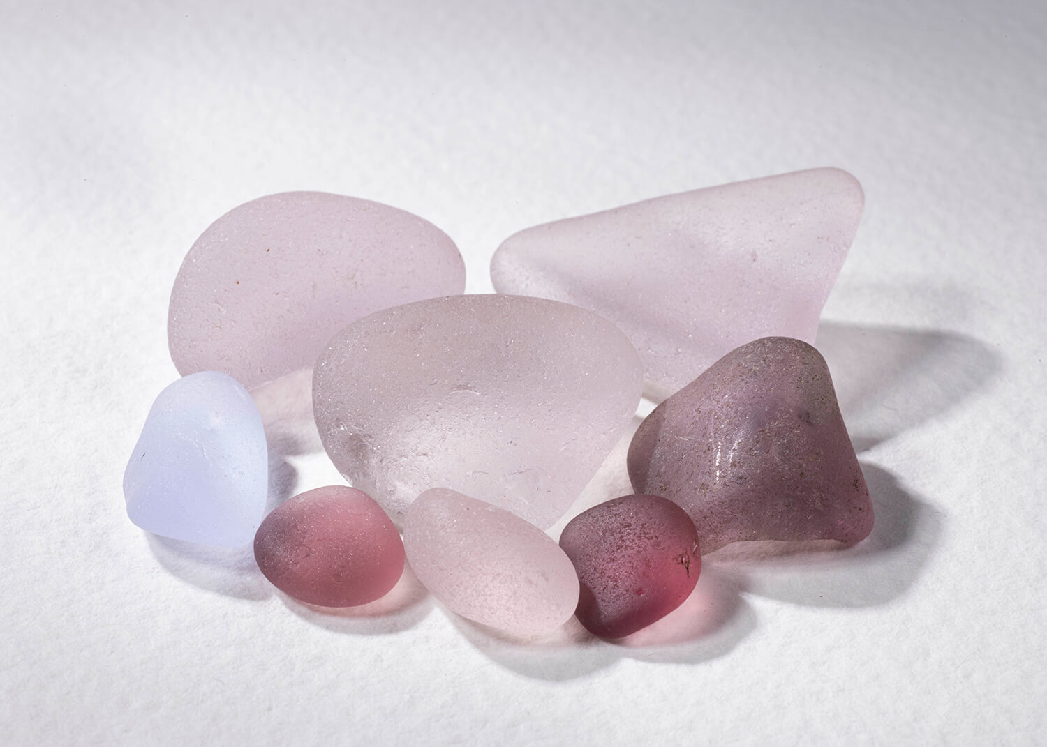 Close up of loose pile of purple sea glass. Some pieces are very dark and some very light. The light is shining through them. By Glasgow jewellery photographers Blink Imaging